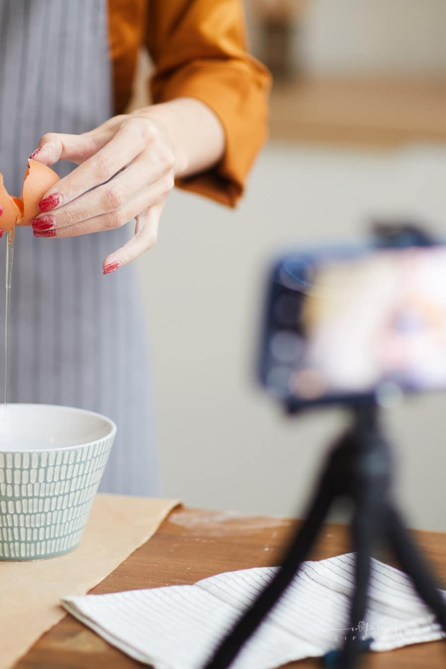 woman cracking open eggs into bowl while  filming baking video