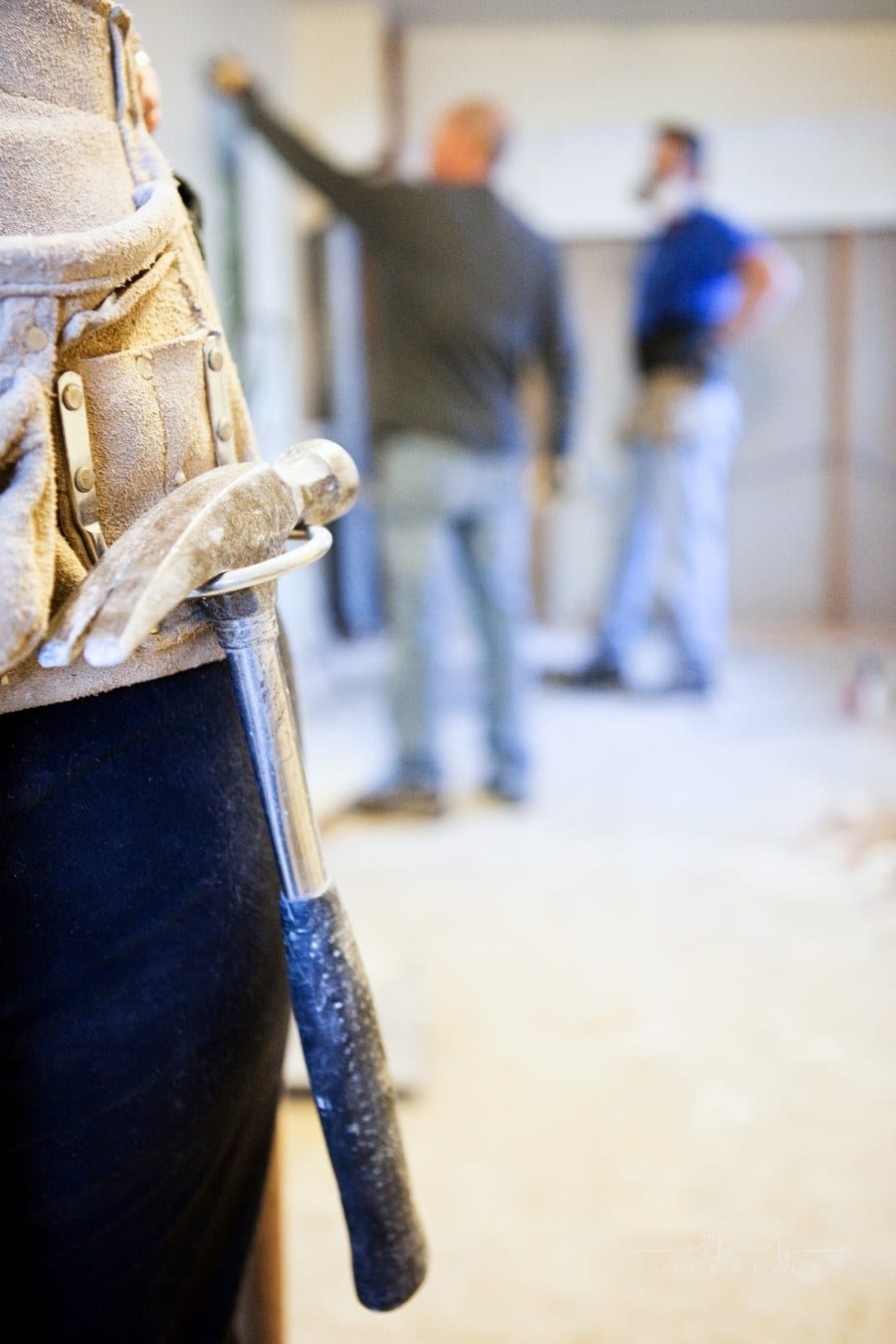 tool belt with hammer hanging down in forefront of two men looking at kitchen renovation
