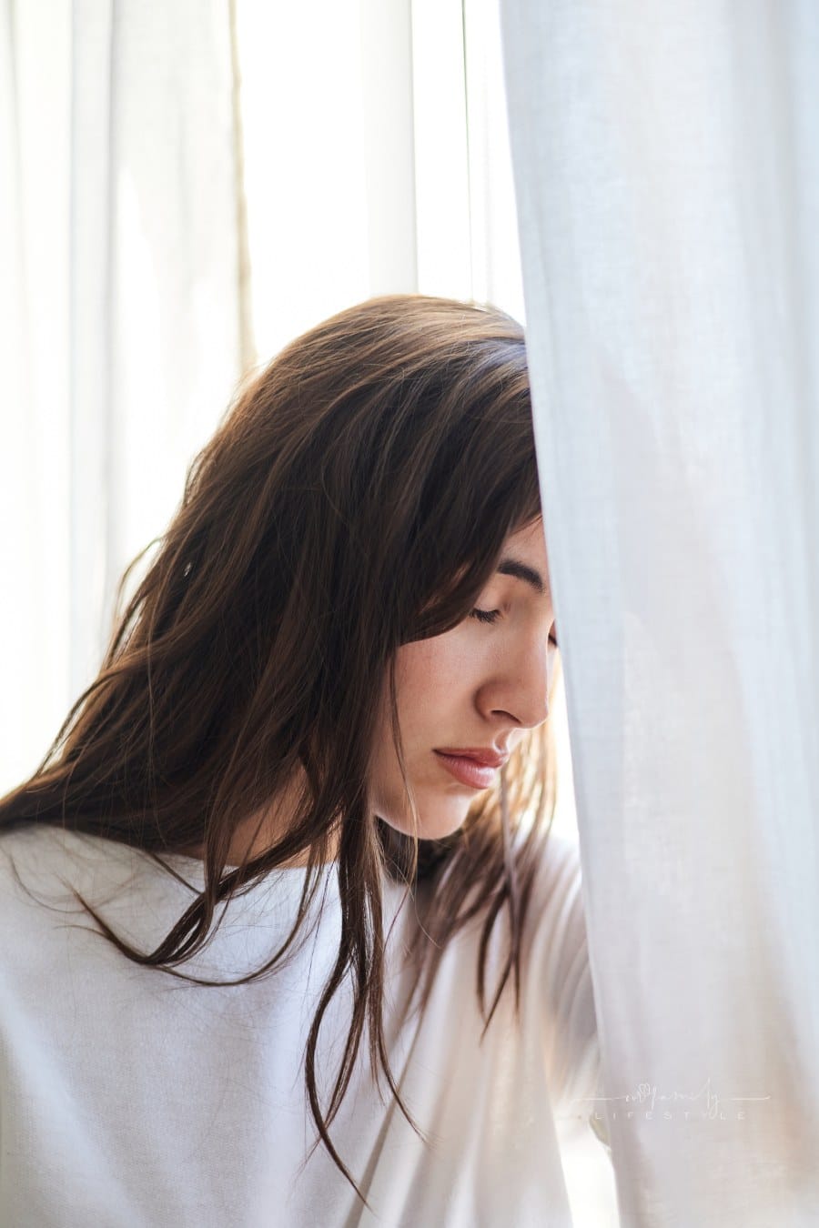 Sad young woman crying by a window at home. Mental health concept.