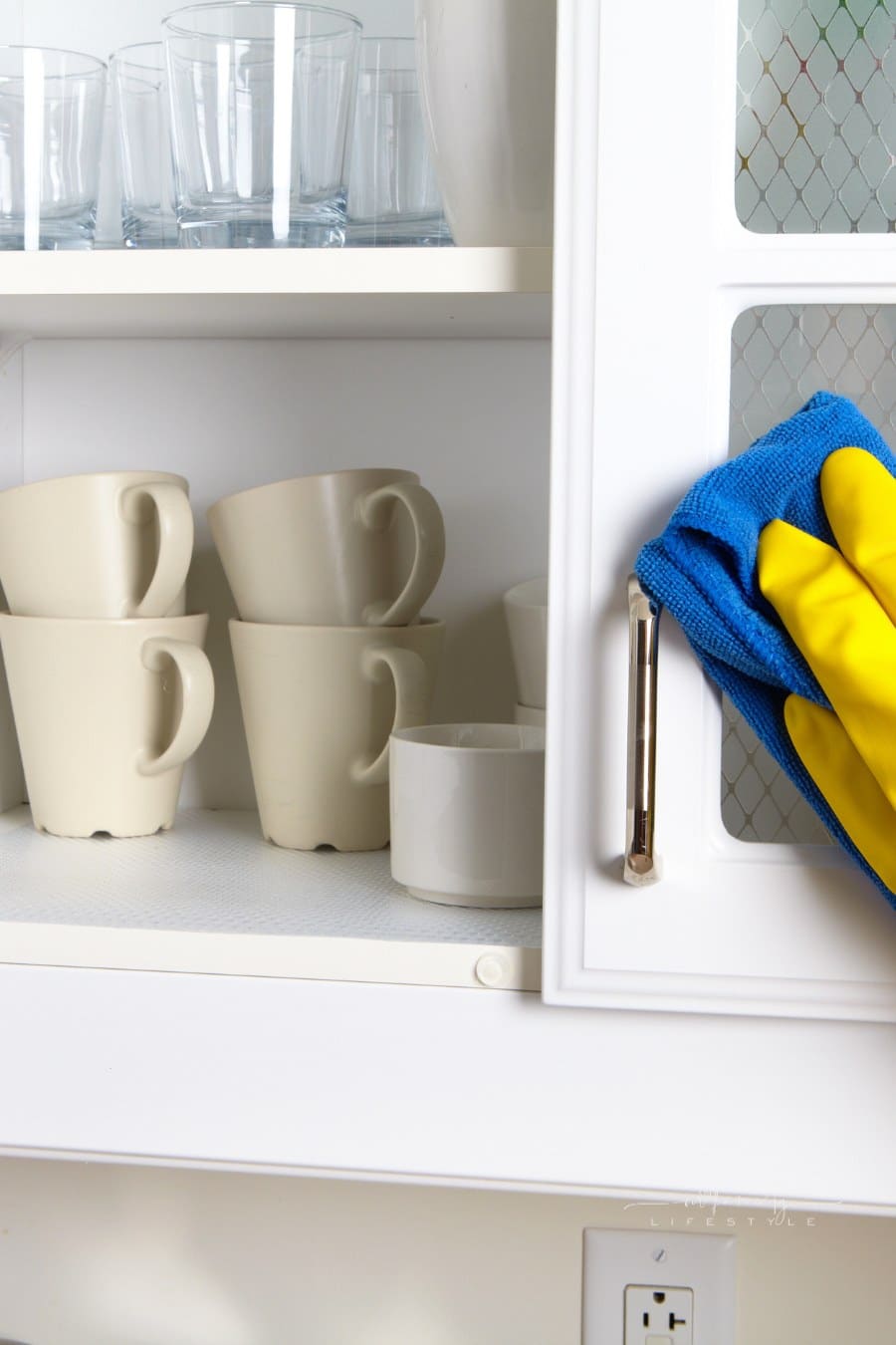 hand dusting cabinets in the kitchen at home with coffee mugs inside , cleaning kitchen cabinets