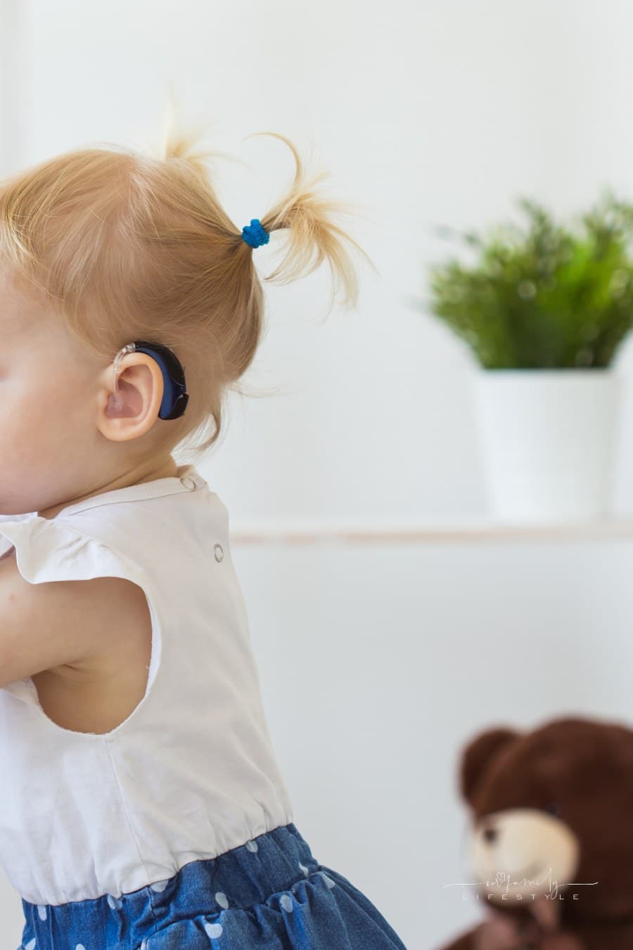 toddler girl wearing a hearing aid while looking out window