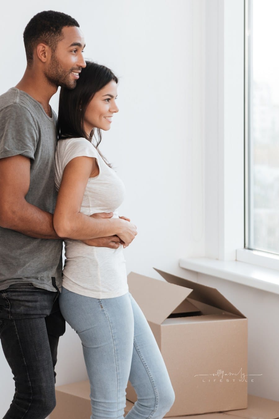 Photo of happy couple hugging while standing near unpacked boxes