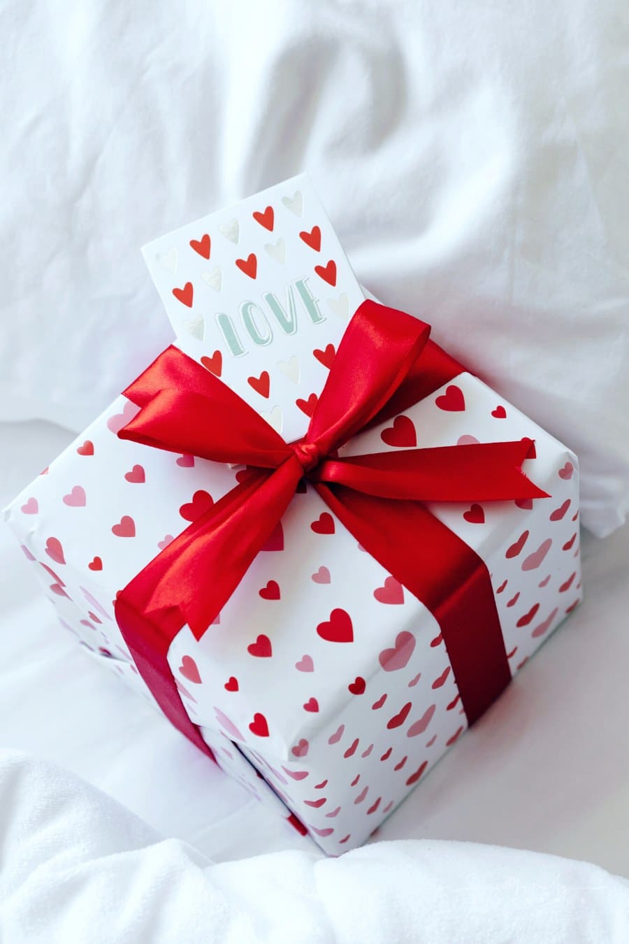 box wrapped in red and white heart wrapping paper with love gift card on a bed of white sheets