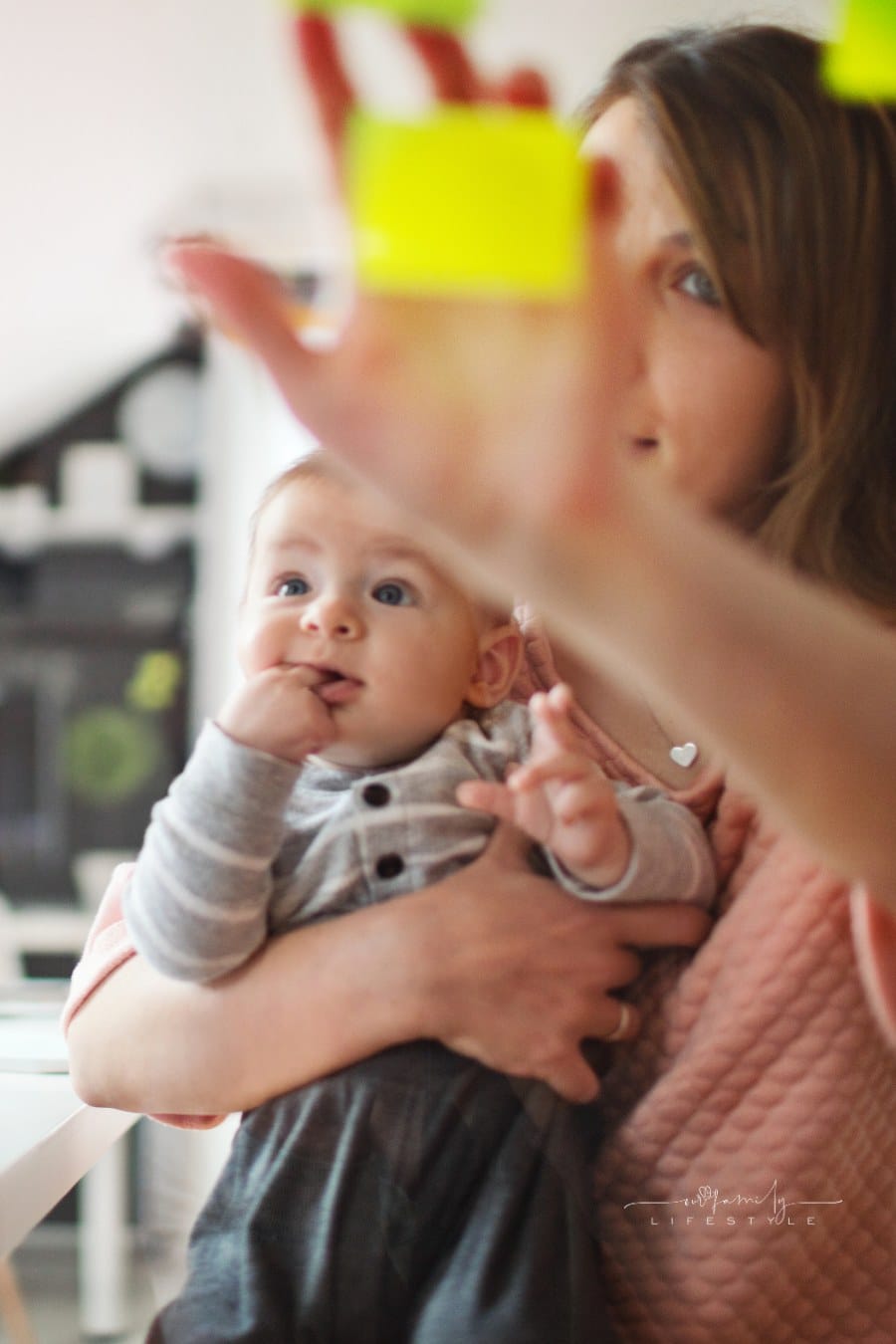 mom working while holding baby and adding sticky notes to wall