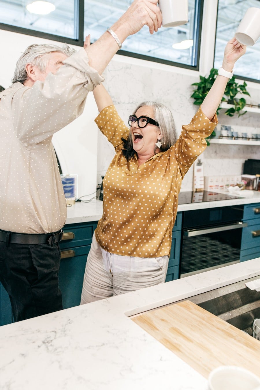 senior couple celebrating in their kitchen with arms raised