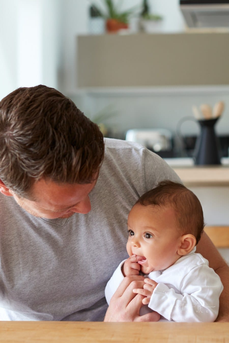 Loving Father Holding 3 Month Old Baby Daughter In Kitchen At Home