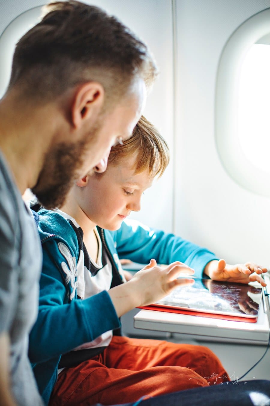 father watching son play with tablet on plane
