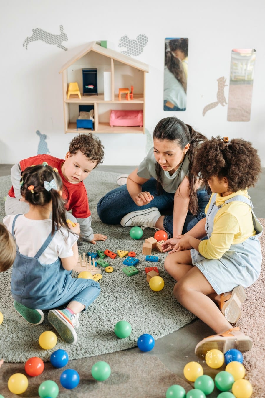 female teacher in Gray Shirt Playing with Preschool Kids on a rug