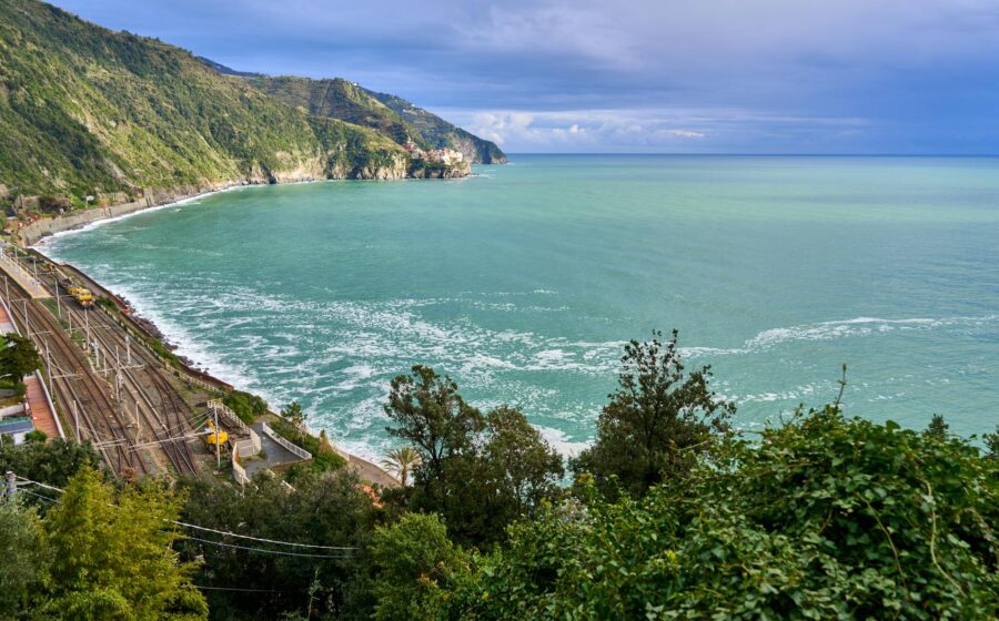 A breathtaking view of the Ligurian coast featuring lush greenery, azure waters, and a railway line along the shoreline.