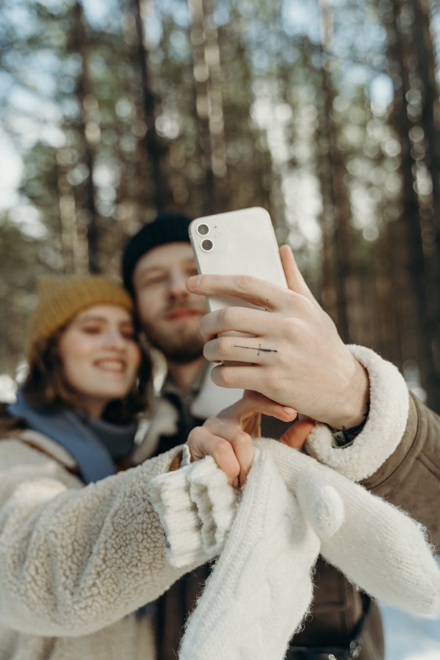 A cheerful couple captures a selfie in a serene winter forest, showcasing warmth and togetherness.