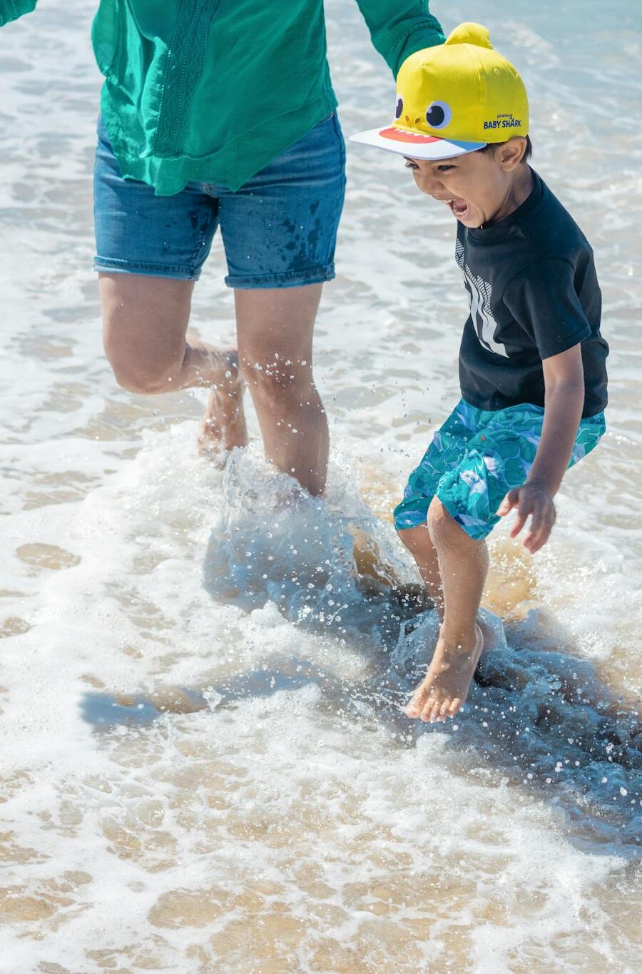A child joyfully splashes in the ocean waves with a parent on a sunny beach day.