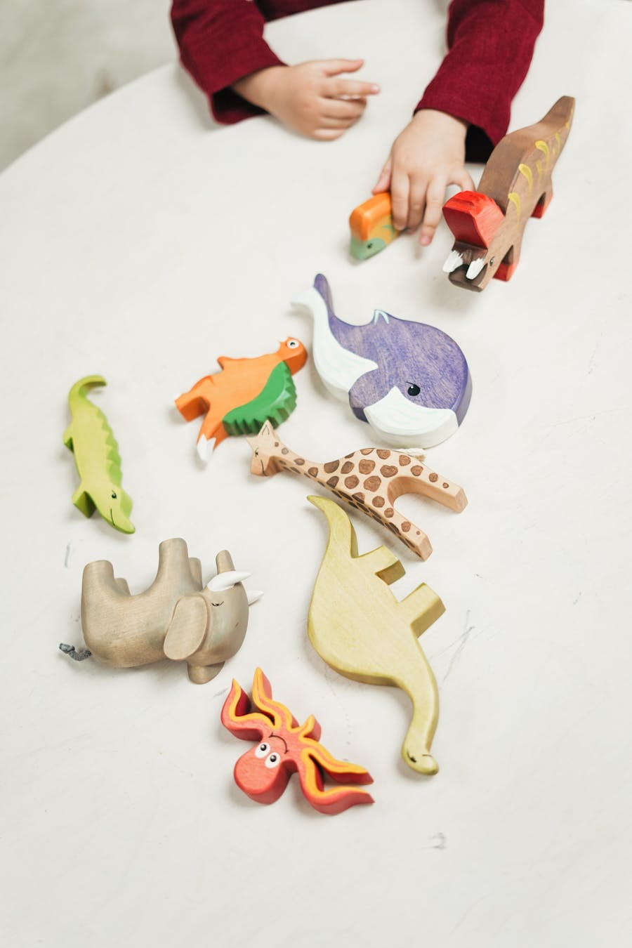 A child plays with a variety of colorful wooden animal toys on a white table indoors.
