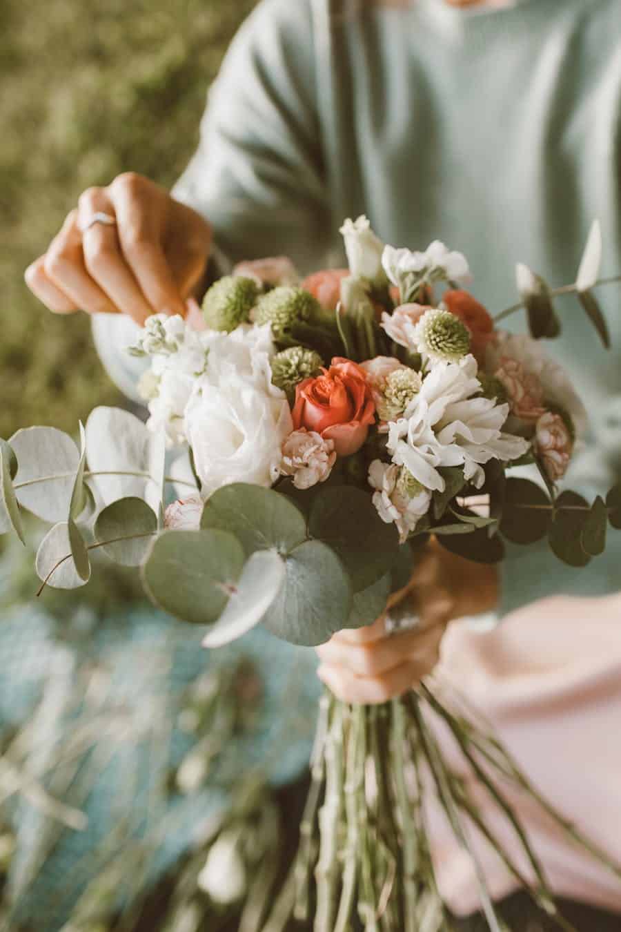 A close-up of hands arranging a beautiful bouquet with roses and greenery.
