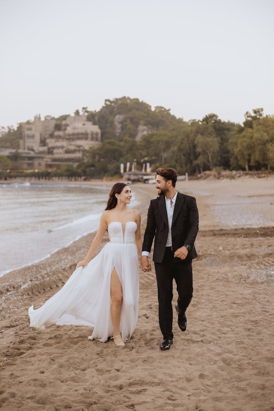A couple enjoying a romantic walk on a sandy beach, dressed in elegant wedding attire.