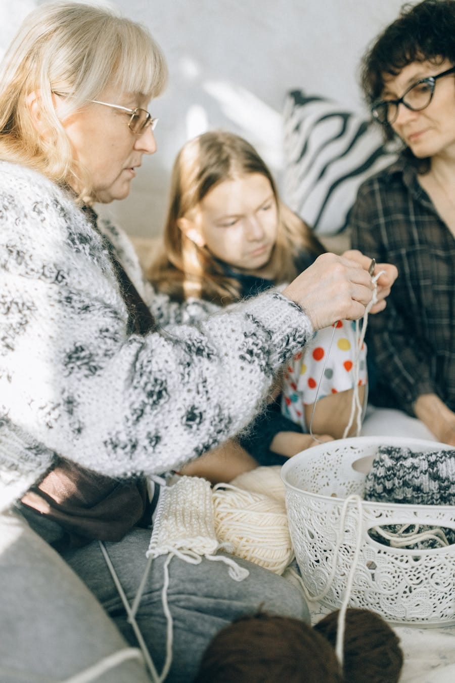 A grandmother teaches crocheting to a child and adult in a cozy indoor setting.