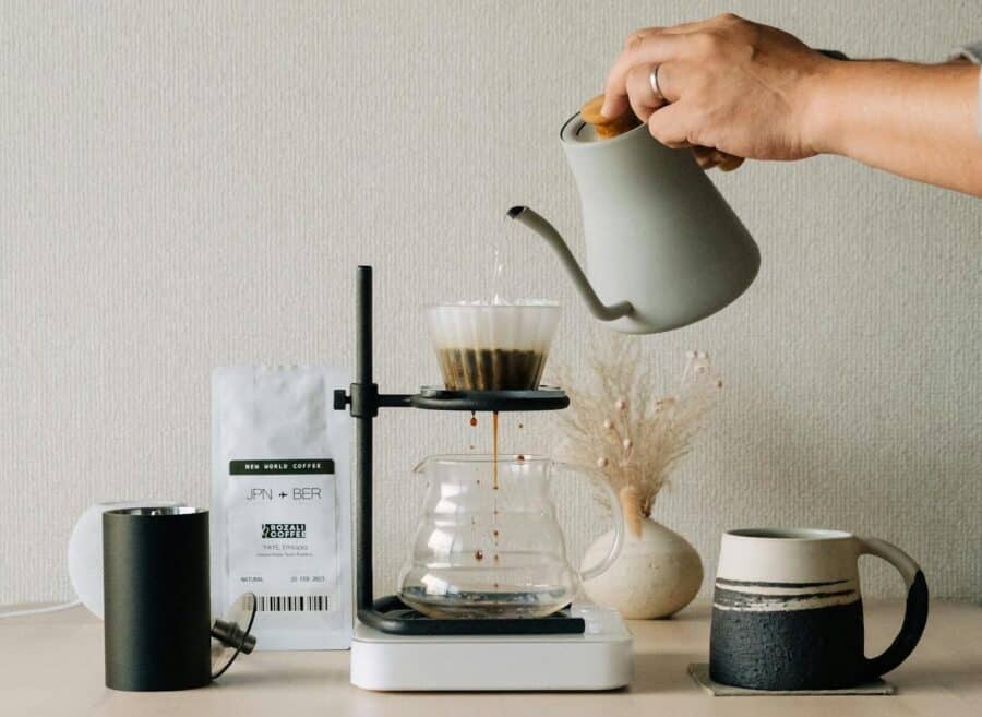 A hand pours water into a coffee filter using a kettle for pour-over brewing setup.