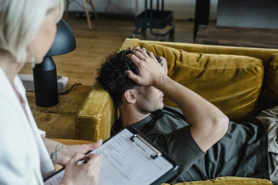 A man lying on a sofa during a therapy session, appearing distressed.