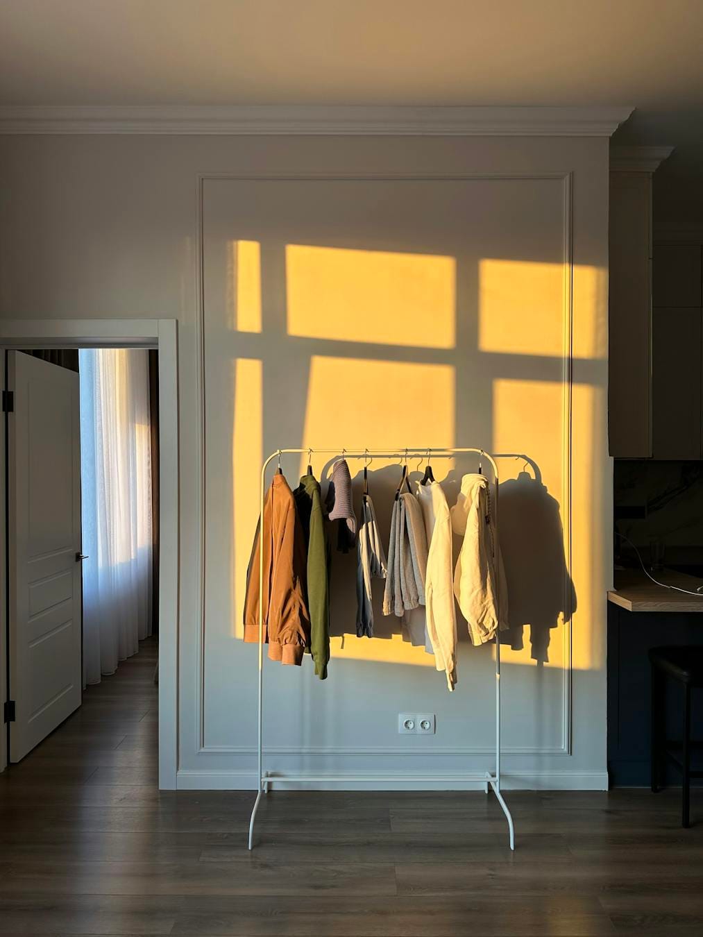 alt="A minimalist interior featuring a clothes rack bathed in warm sunlight casting dramatic shadows."