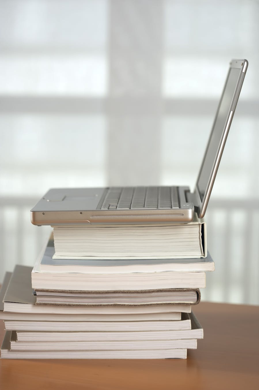 A modern laptop placed on a stack of books indoors, suggesting learning or work.