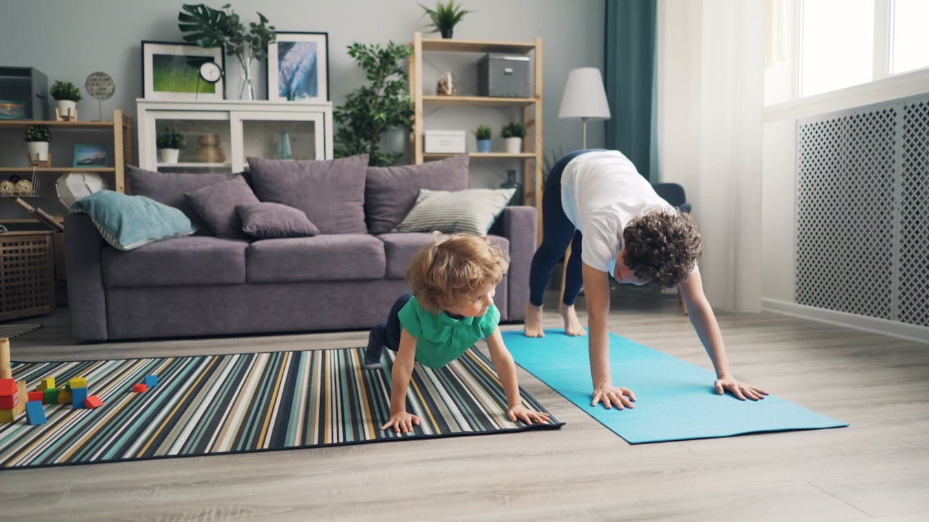 A mother and her child practice yoga together in a cozy living room setting. Family fitness at home.