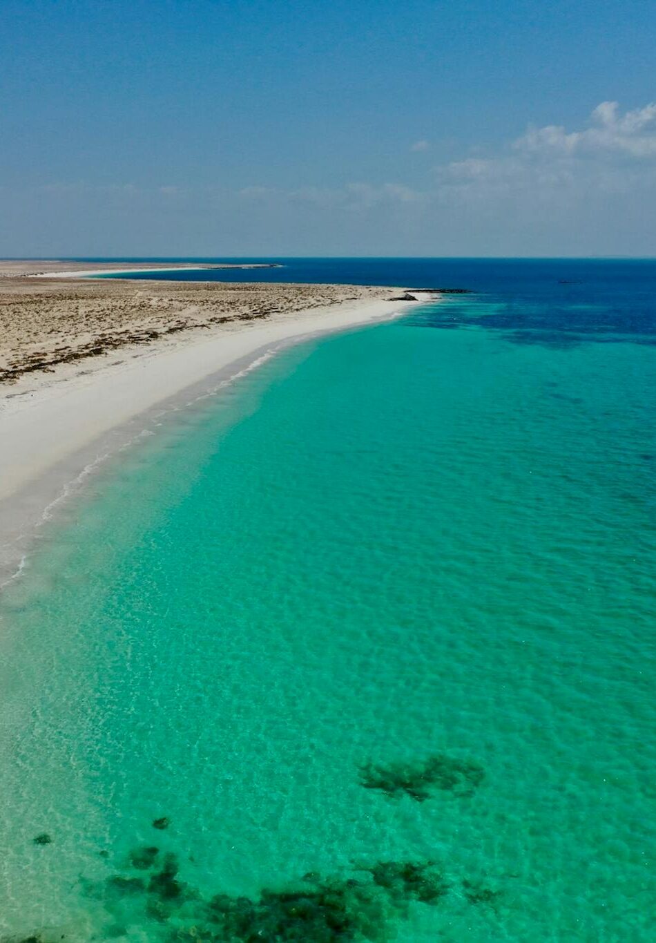 A serene deserted beach with turquoise waters and a clear sky in Oman.