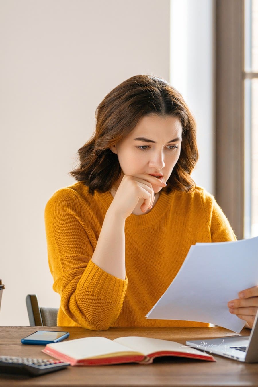 woman staring diligently at paper in frront of laptop