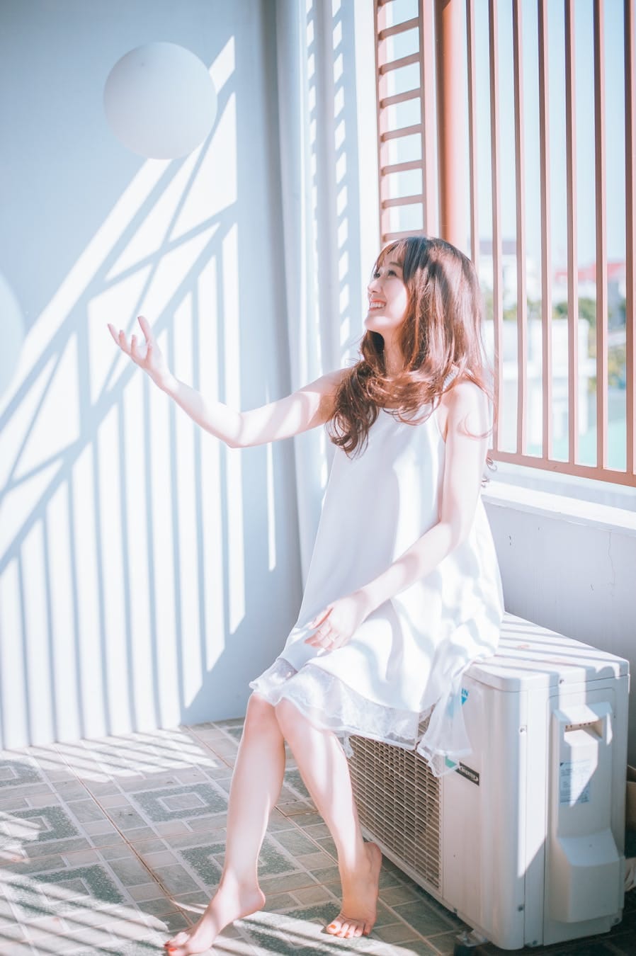 A young woman in a white dress enjoying playful sunlight indoors.
