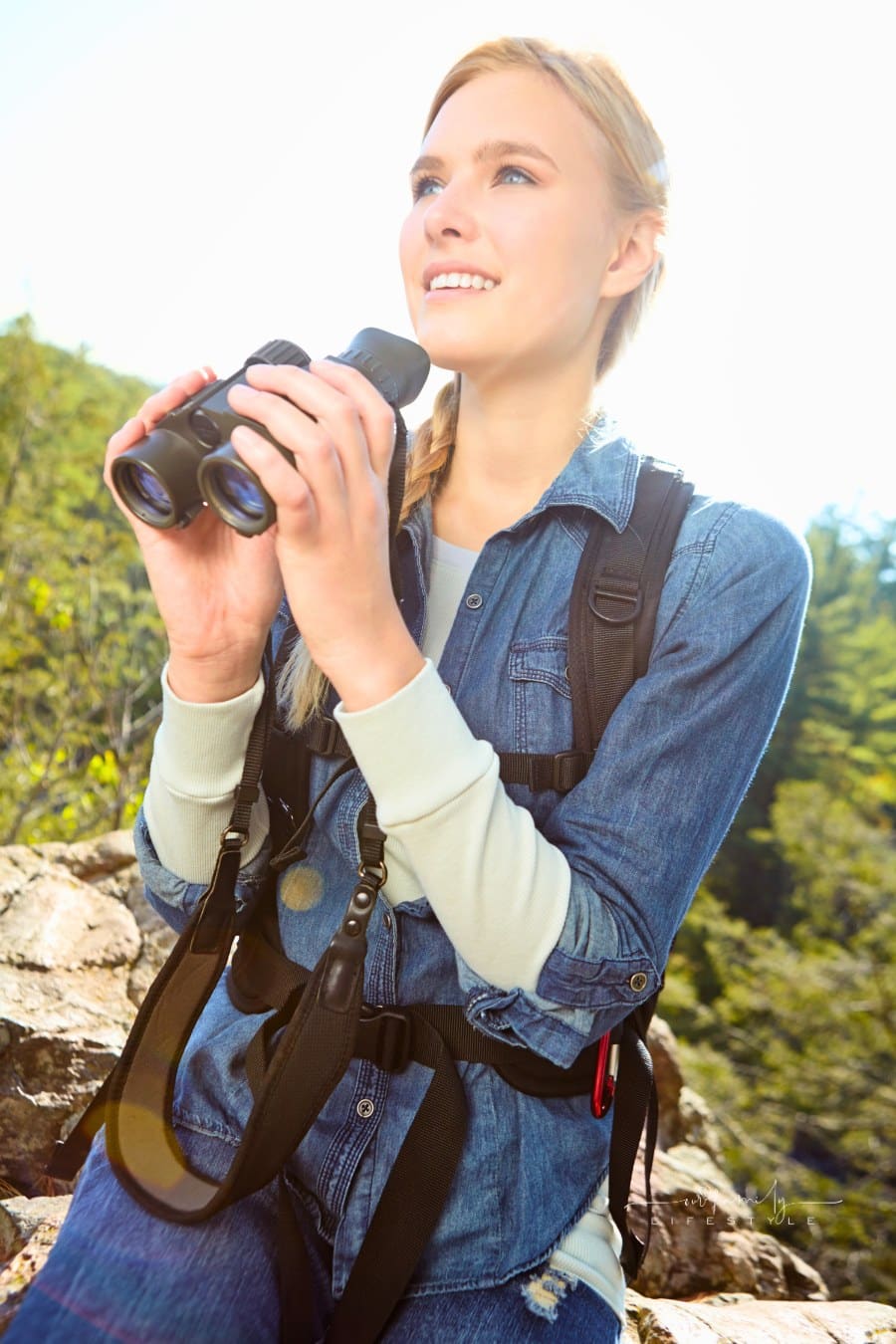 A young woman holding her binoculars while atop the mountainside