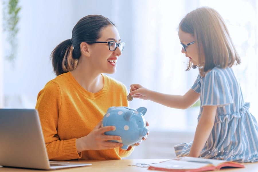 Woman Calculating Family Budget with daughter putting coins in piggy bank