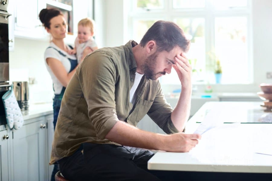 dad unhappy while looking over family finances with mom and baby in background