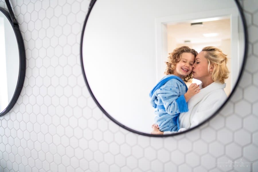A reflection of mother and small daughter in mirror in bathroom indoors at home.