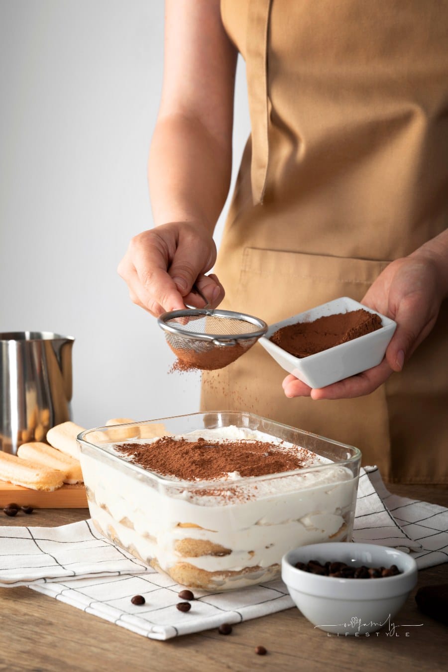 hand dusting the tiramisu with cocoa powder using a strainer