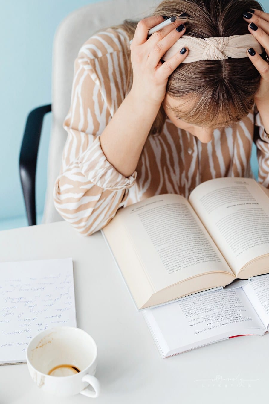woman holding her head in her hands while studying stack of books