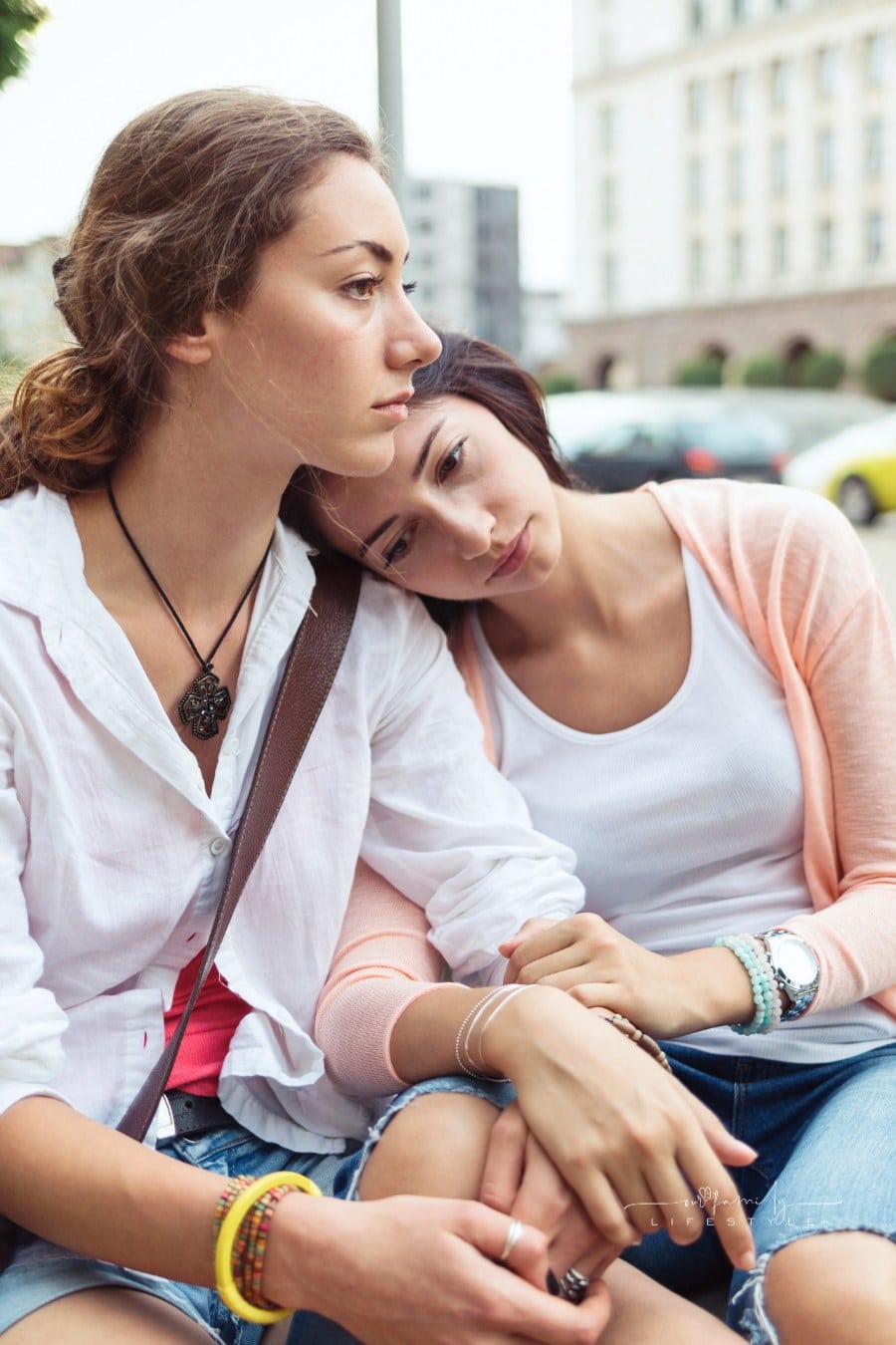 two unhappy friends holding each other while sitting on city bench