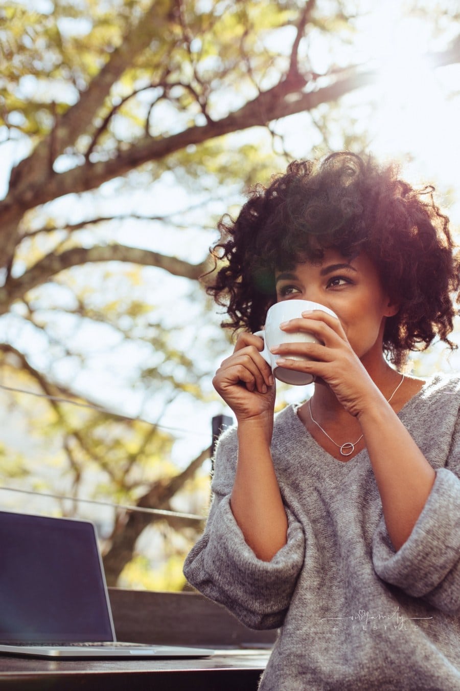 Curly haired woman sitting outdoors with coffee cup in her hands. Happy young woman sitting outdoors with a laptop and coffee.