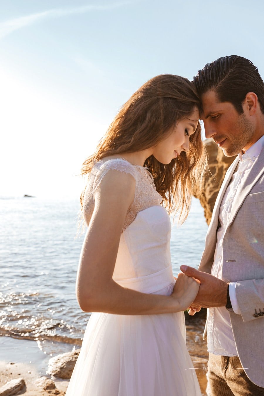 bride and groom holding hands with heads touching in front of ocean