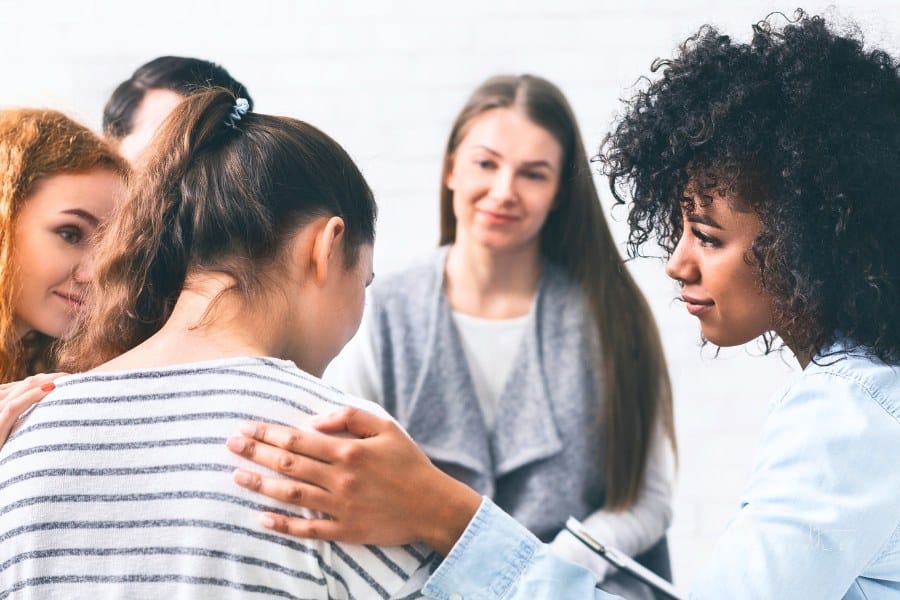 Support group patients comforting woman at therapy session