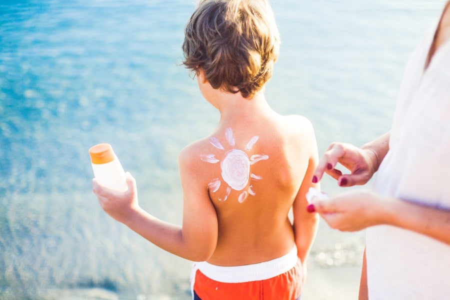 mom putting sunscreen on child's back at beach
