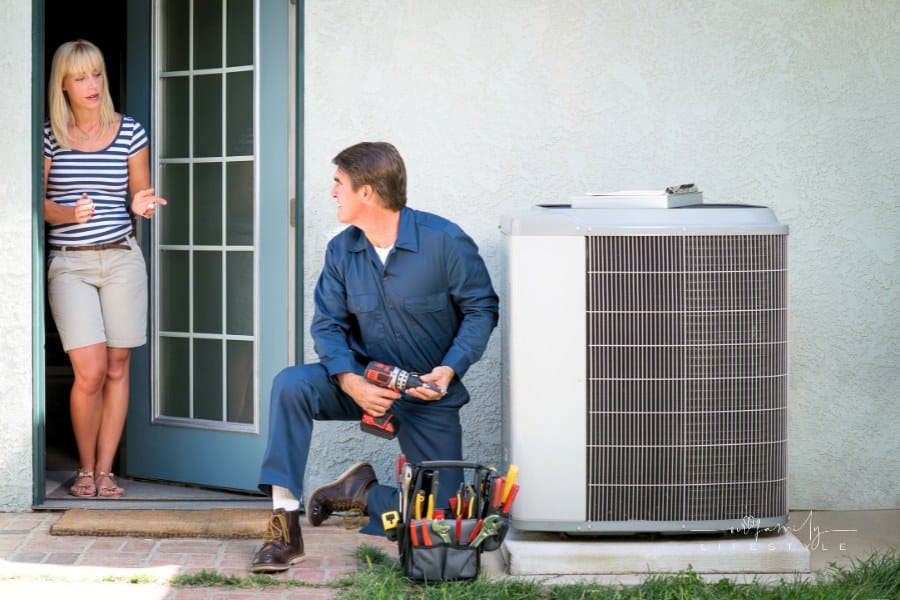 Air conditioner repairman in uniform, discussing with the female homeowner the unit's repair.