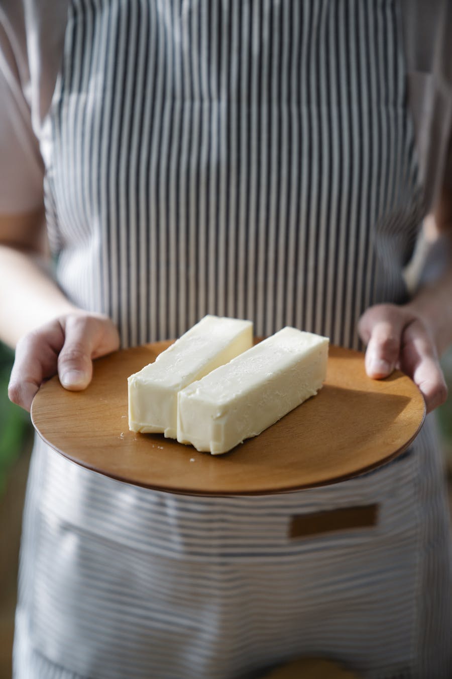 Close-up of a chef holding a wooden plate with two sticks of butter.