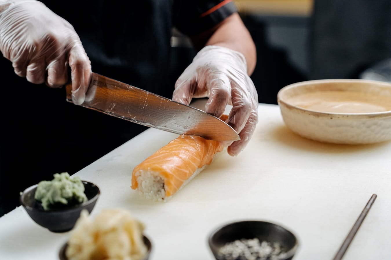 Close-up of a chef slicing a salmon sushi roll with precision, showing fresh ingredients.