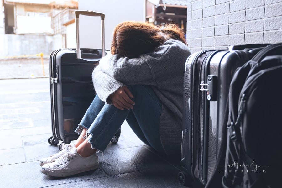 A sad, frustrated woman sitting on the floor while traveling with a lot of baggage