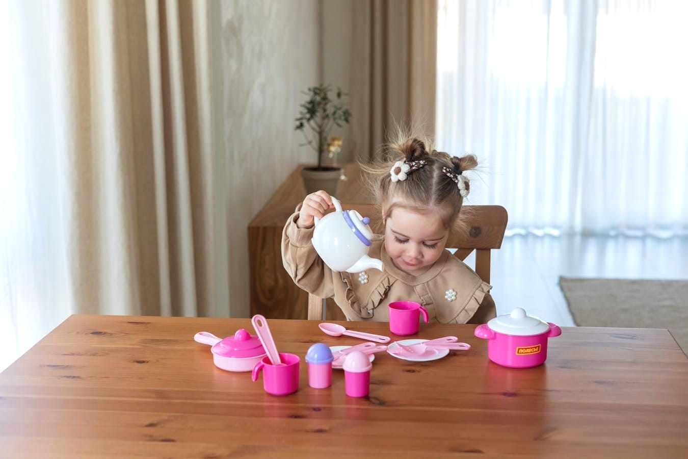 Cute young girl having fun with a toy tea set on a wooden table indoors.
