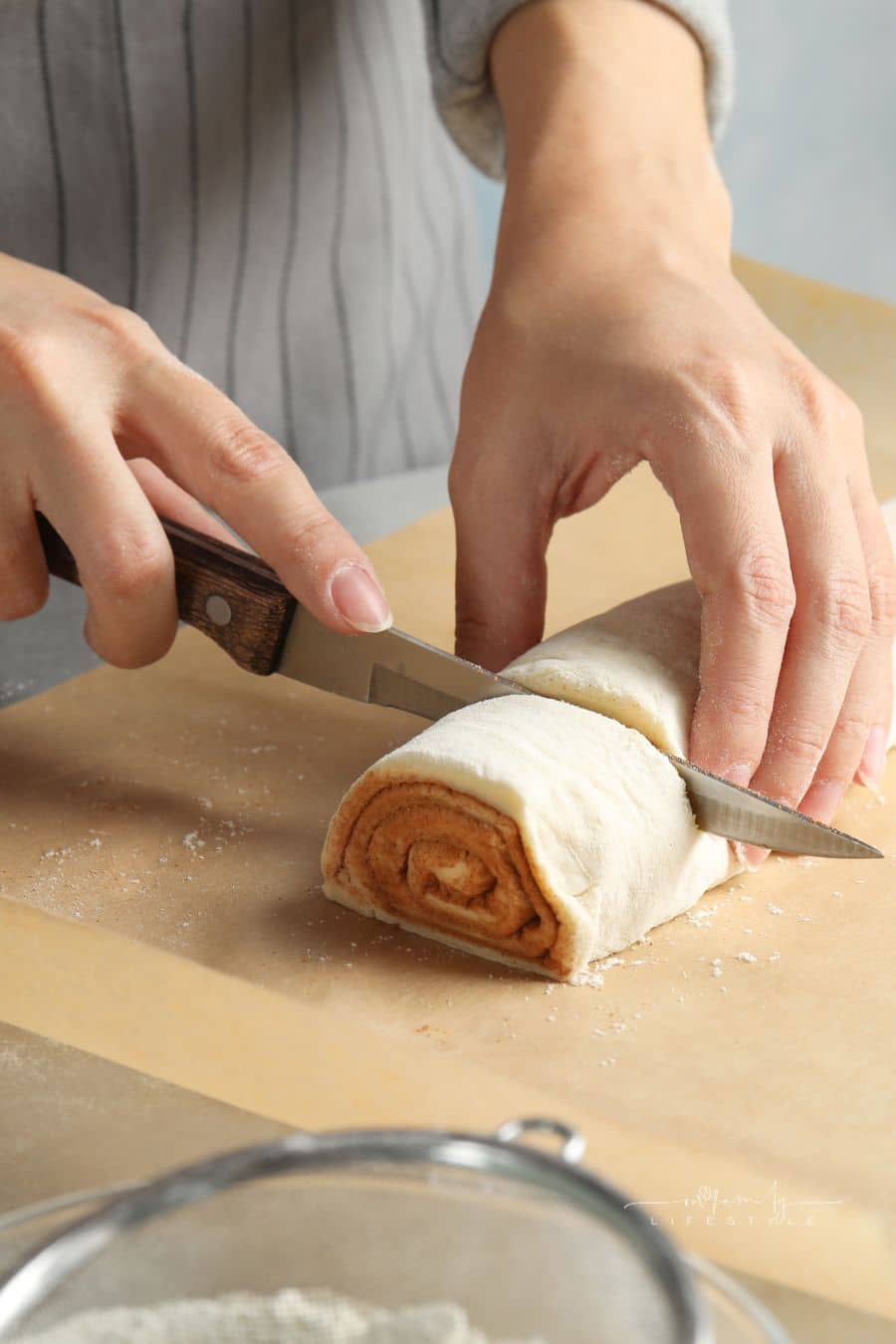 Woman Making Cinnamon Rolls at Table, Closeup; cutting rolled dough to form cinnamon roll