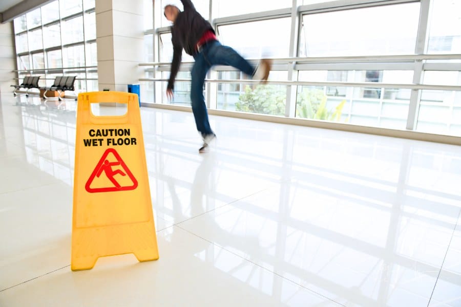 Man slips falling on wet floor next to the wet floor caution sign.