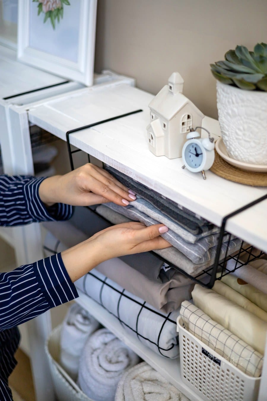 woman in pajamas neatly putting folded linens into cupboard vertical storage Marie Kondo