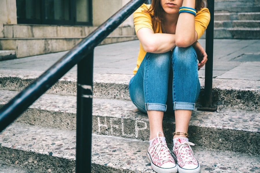 depressed teen girl sitting on stairs and holding her head in her hands