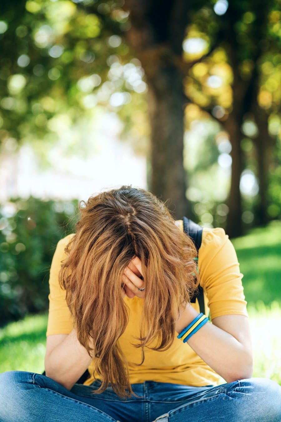 depressed teen girl sitting on sidewalk and holding her head in her hands