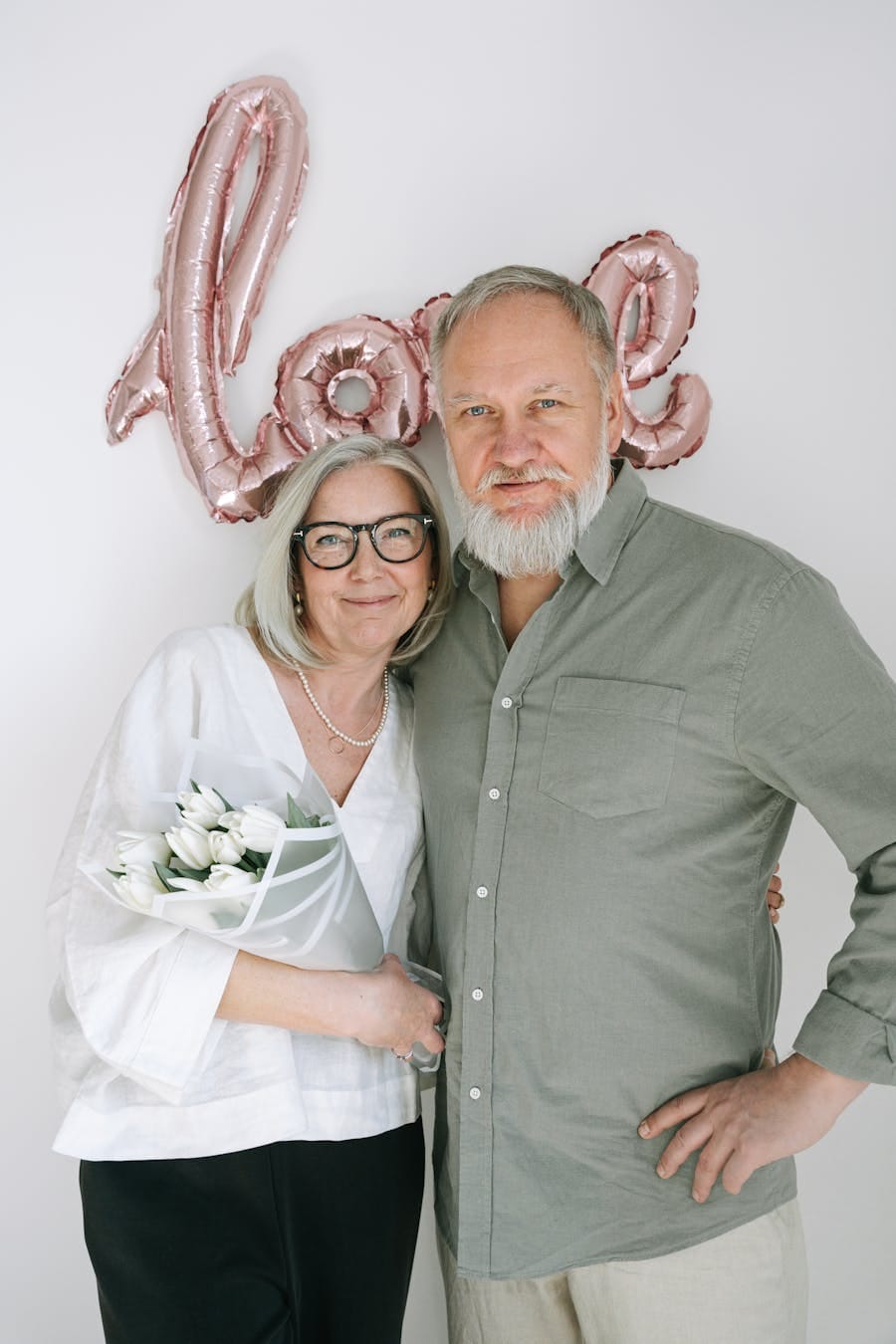 Elderly couple embraces and celebrates love with a bouquet of tulips indoors.
