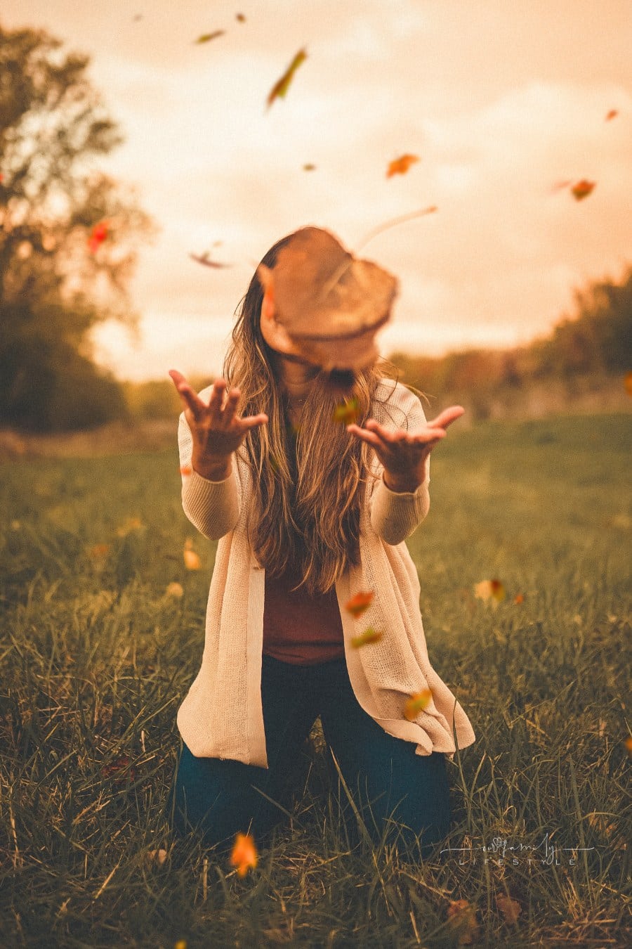woman in autumn countryside at sundown throwing fall leaves into air